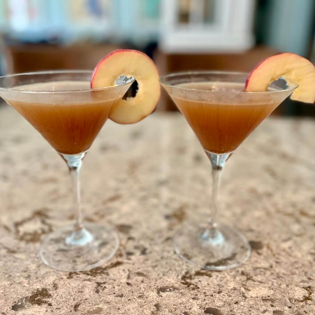 Two martini glasses filled with buttered apple rum, garnished with sliced apples