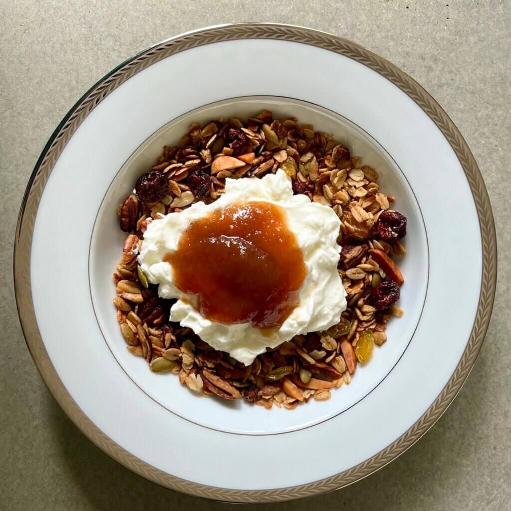 A white bowl filled with homemade granola, topped with Greek yogurt and New Canaan Farms Country Apple Butter