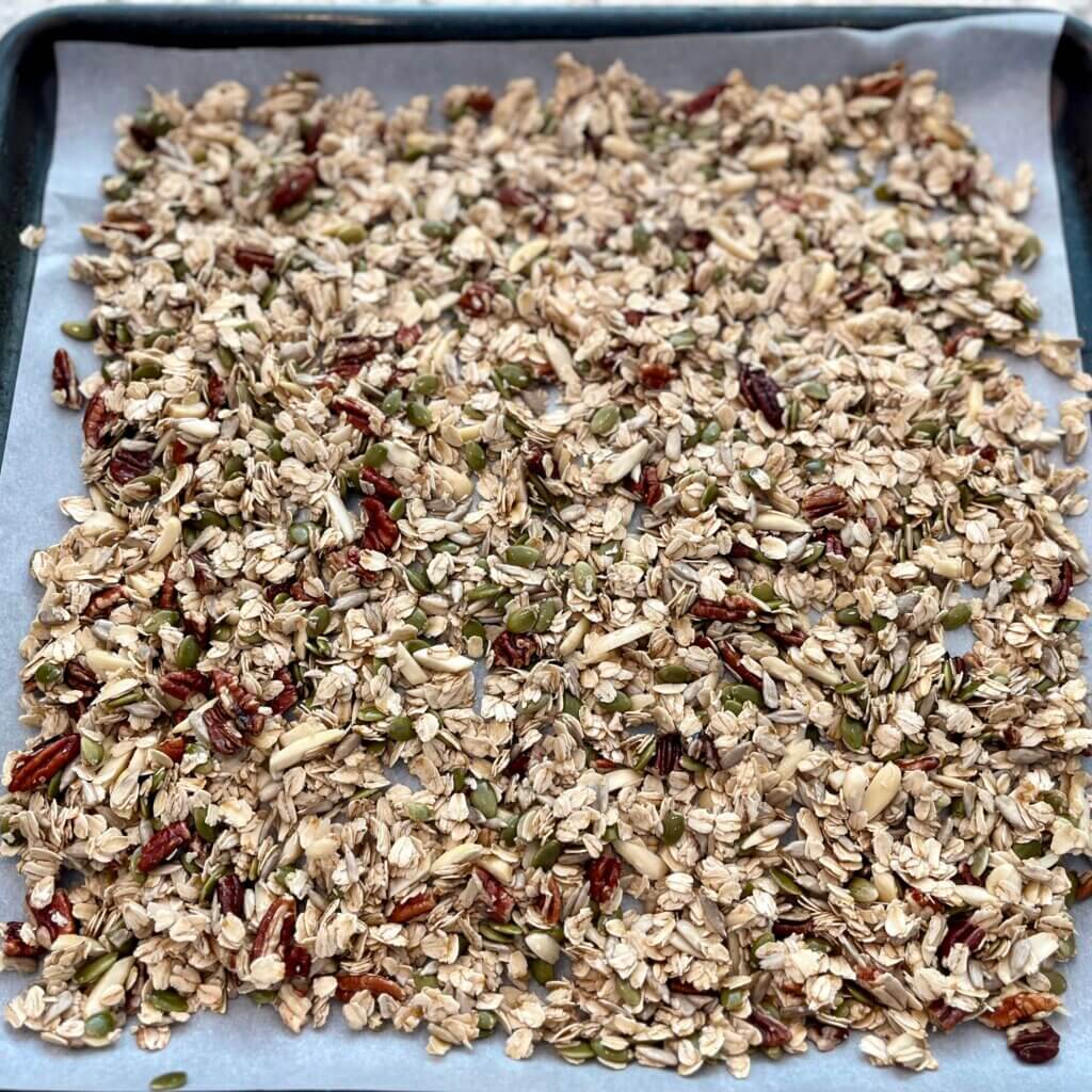 A large baking pan spread with a piece of parchment paper and filled with uncooked granola 