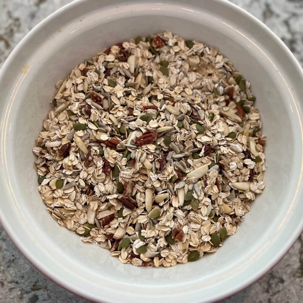 A large white bowl of raw rolled oats, seeds and nuts