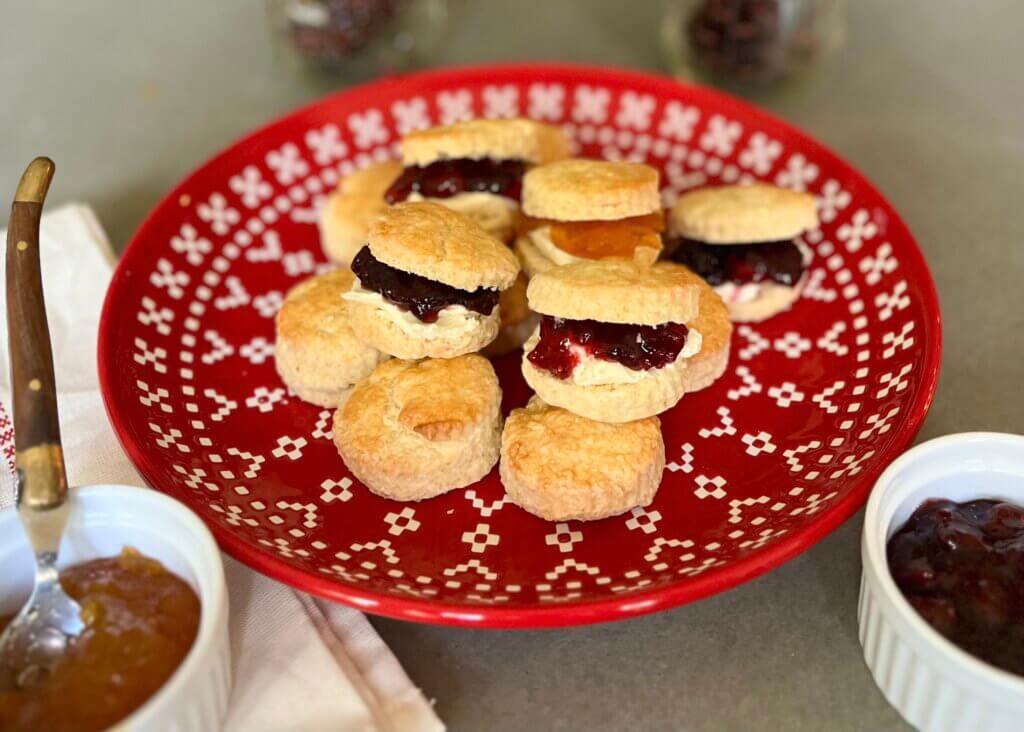 A red plate containing several mini scones, filled with fresh cream and an assortment of New Canaan Farms jams