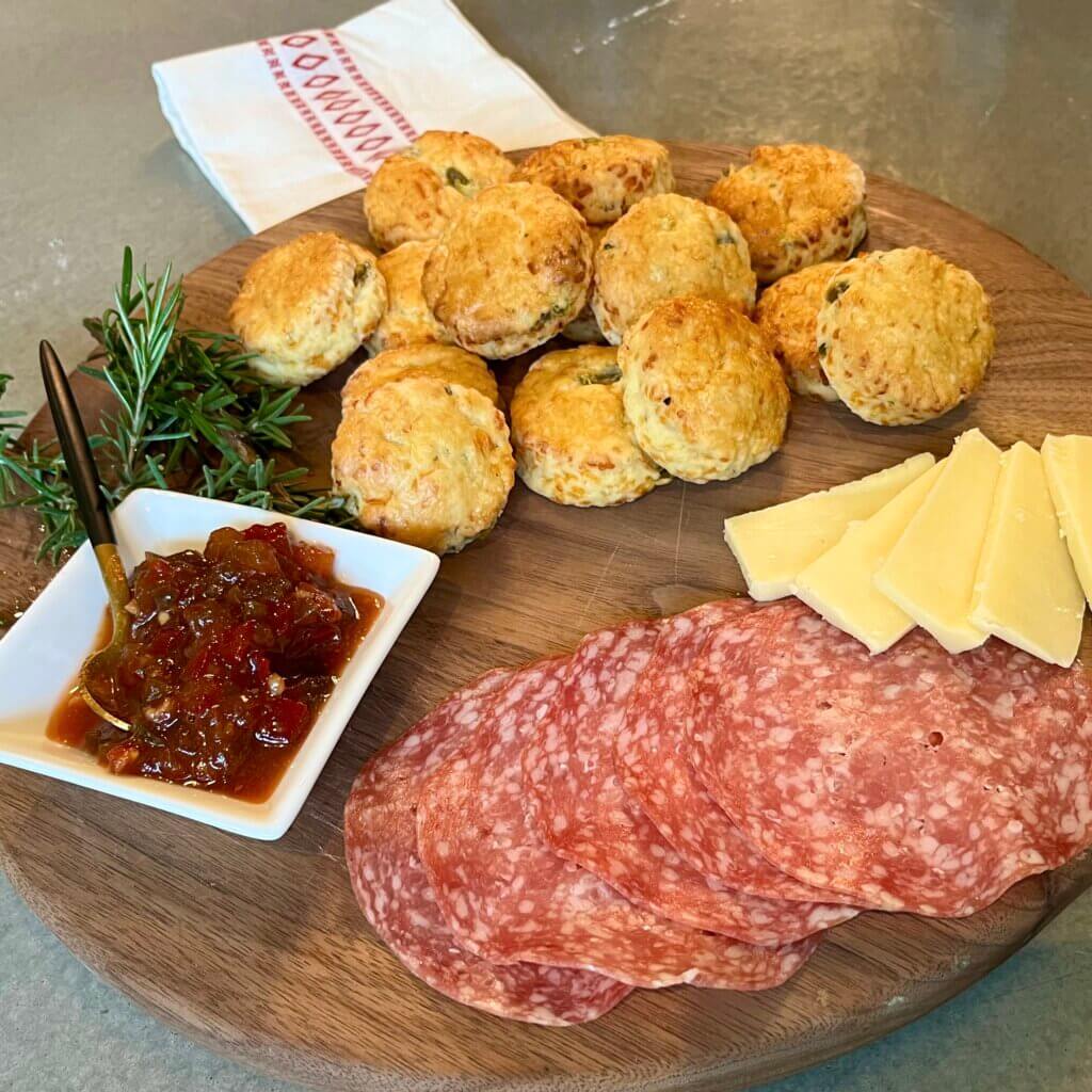 A charcuterie board with salami, cheese jalapeño scones and New Canaan Farms Pepper Bacon Relish