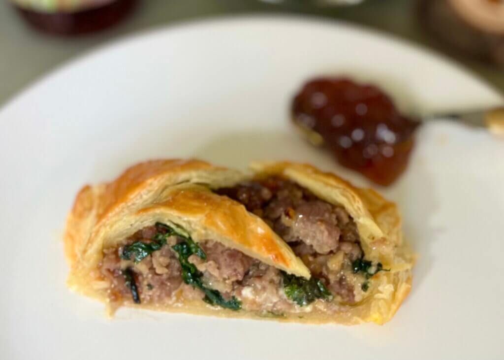 A white plate with a slice of gourmet sausage roll and New Canaan Farms Onion & Garlic Jam