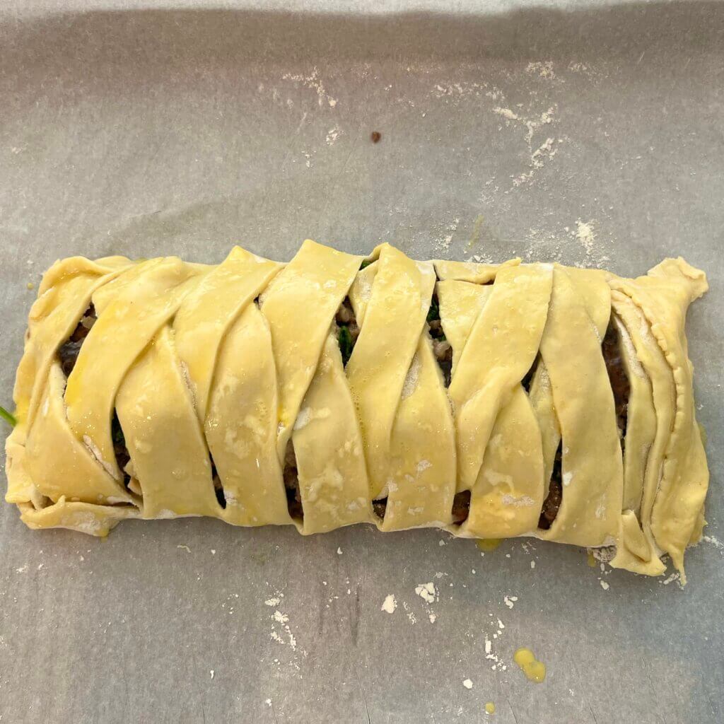 Large festive sausage roll made with puff pastry about to go into the oven