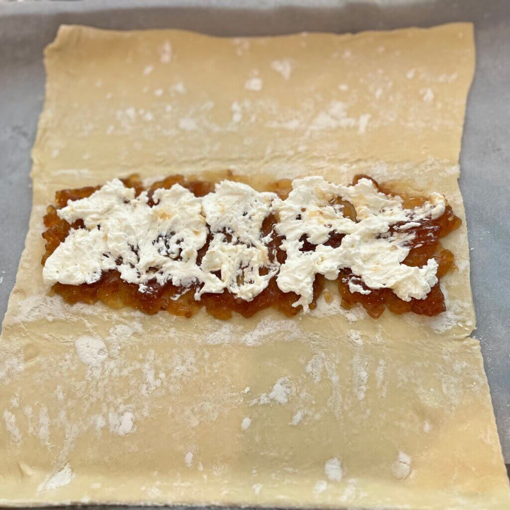 A rolled out sheet of puff pastry, with the center third spread with New Canaan Farms Caramelized Onion & Garlic Jam, and dotted with cream cheese
