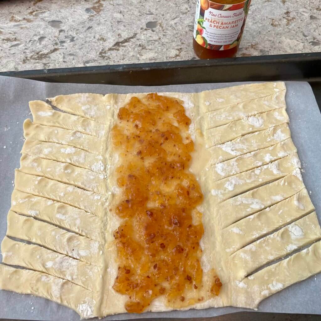 A sheet of uncooked puff pastry with New Canaan Farms each Pecan & Amaretto Jam spread down the middle