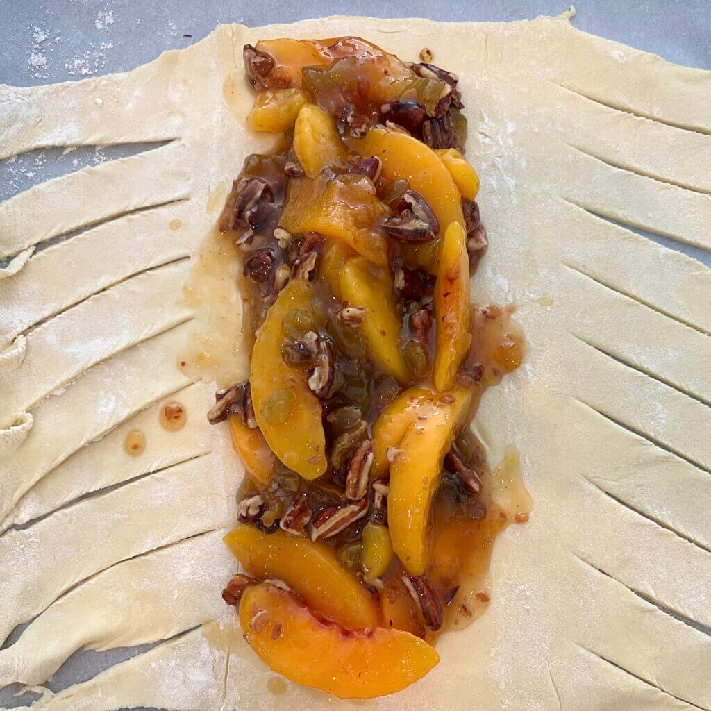 Uncooked puff pastry with the middle third piled with peaches, pecans and New Canaan Farms Peach Pecan & Amaretto Jam