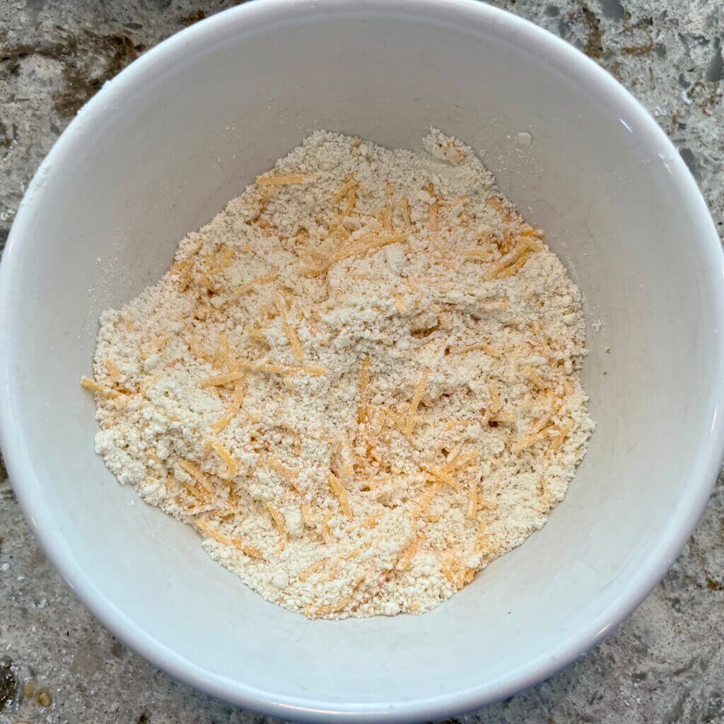 A white bowl filled with flour, butter and cheese for a cheese scone base