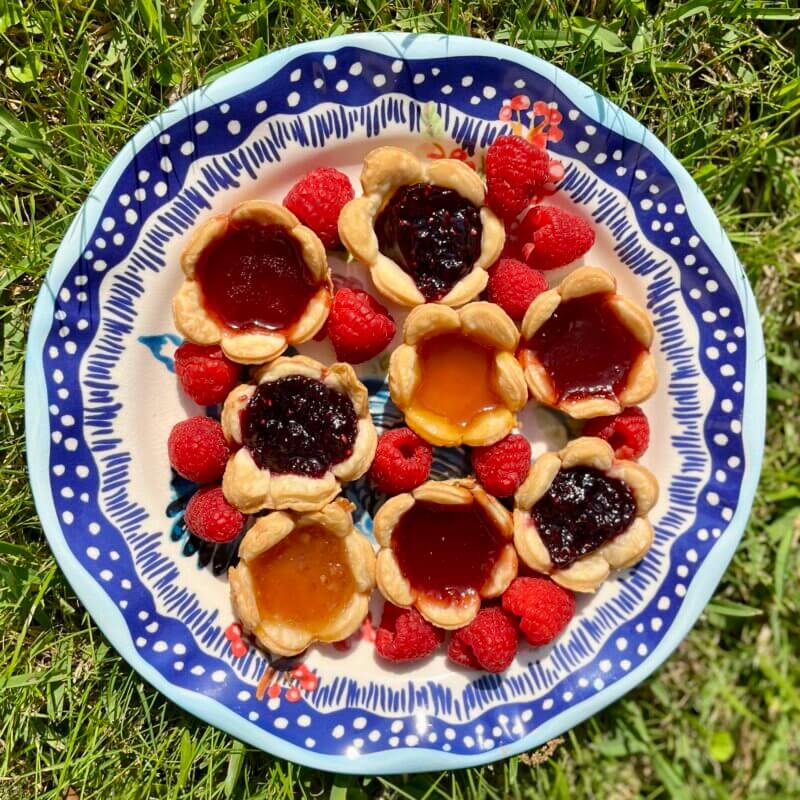 A plate of jam tarts containing New Canaan Farms Blackberry, Peach and Strawberry Almond jams