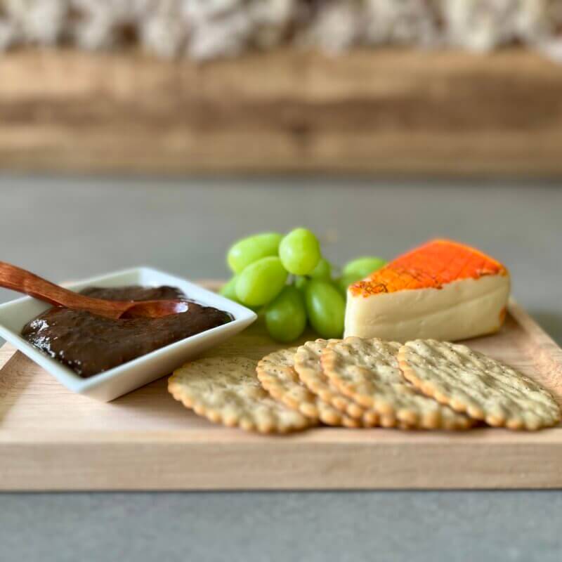 New Canaan Farms Balsamic Dijon Mustard on a wooden board with some crackers and cheese