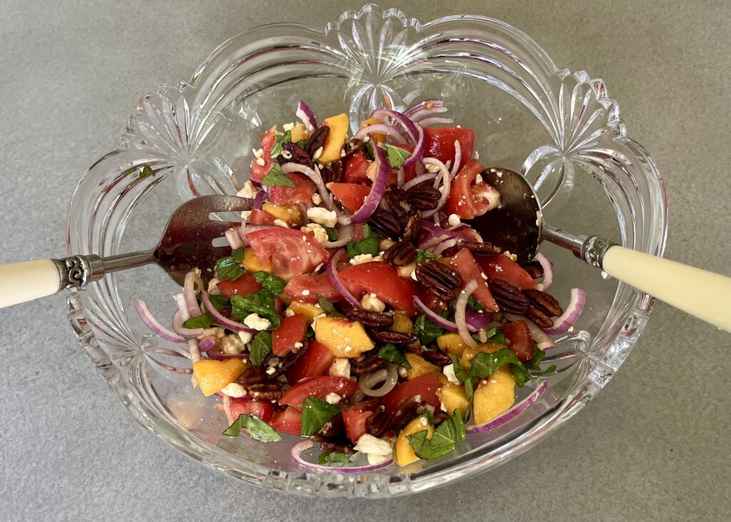 A glass bowl containing a summery tomato peach salad, dressed with new Canaan Farms Mango Habanero Sauce