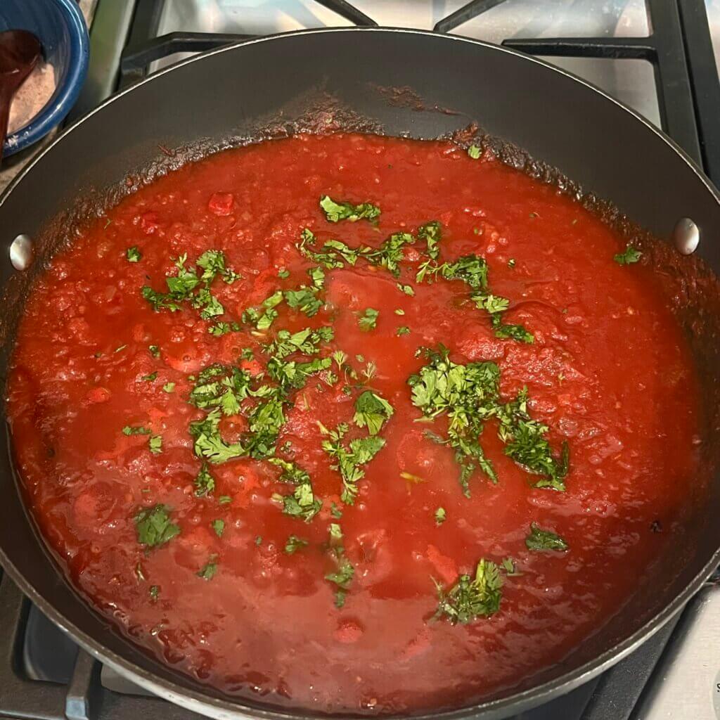 A pan on the stove simmering New Canaan Farms Pedernales Picante Sauce, with chopped cilantro on top