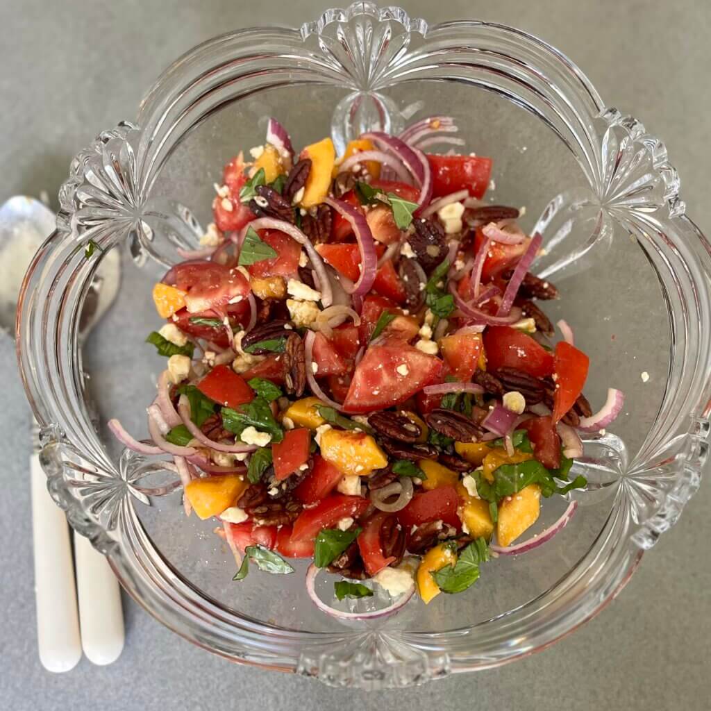 An arial view of a glass bowl containing a tomato and peach salad, with New Canaan Farms Mango Habanero dressing