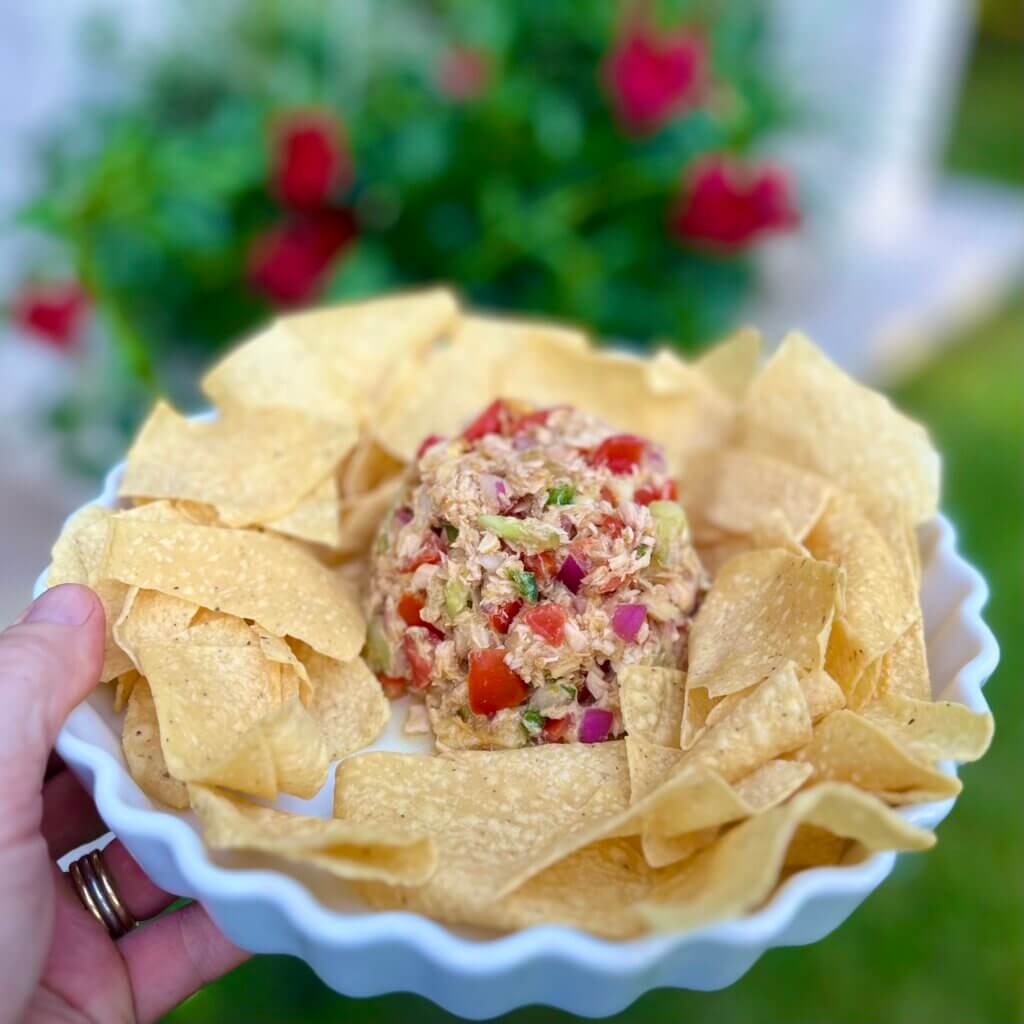 A hand holding a white platter containing salmon ceviche salad made with New Canaan Farms Mango Habanero Sauce, surrounded by tortilla chips