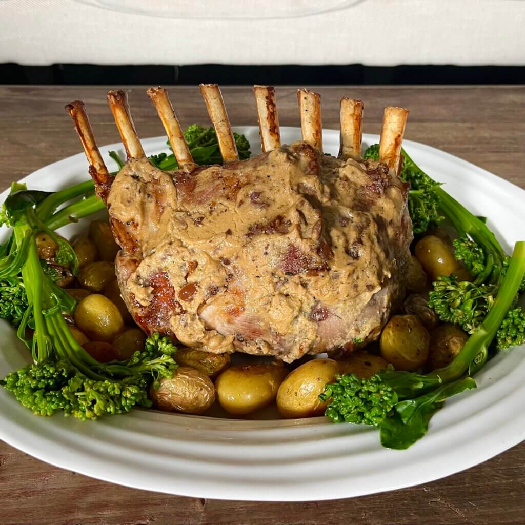 A rack of lamb, basted with New Canaan Farms Olive Rosemary Dijon Mustard, surrounded by roasted potatoes and broccolini