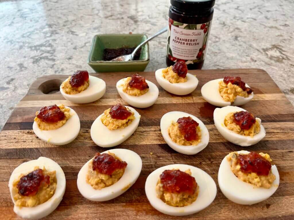 Deviled eggs topped with New Canaan Farms Cranberry Pepper Relish on a wooden cutting boar