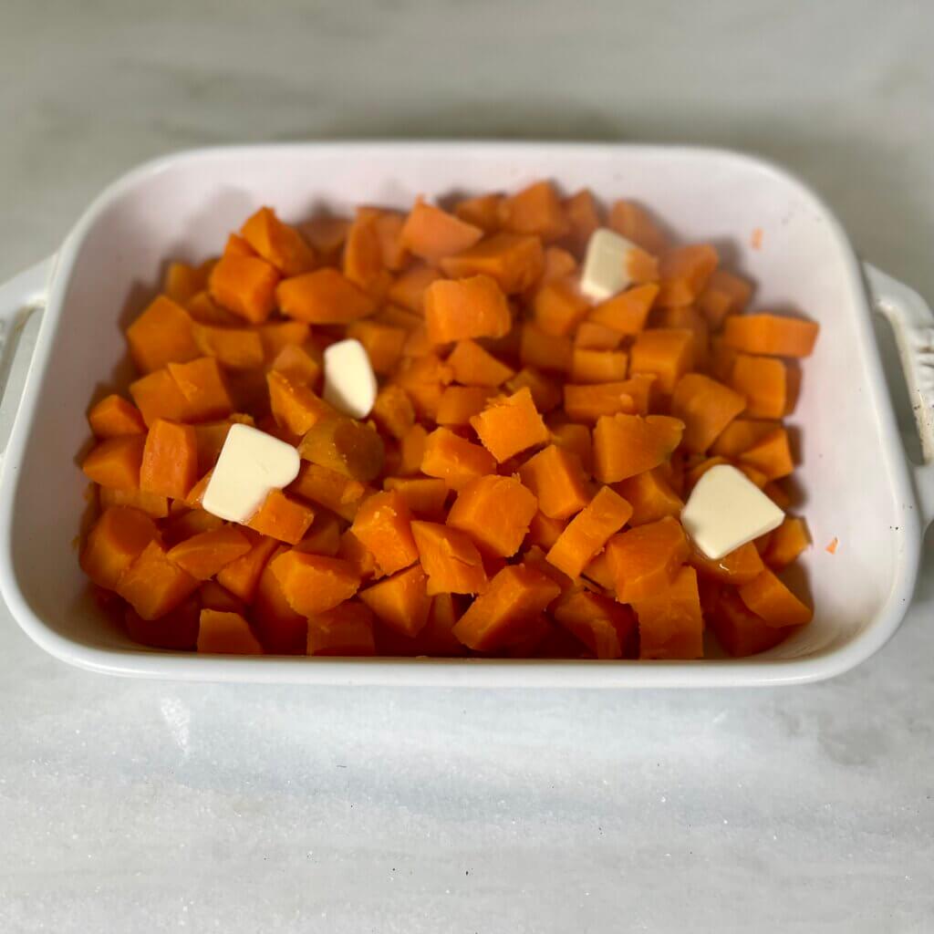 Par-boiled cubed sweet potatoes in a white casserole dish, topped with a few pats of butter