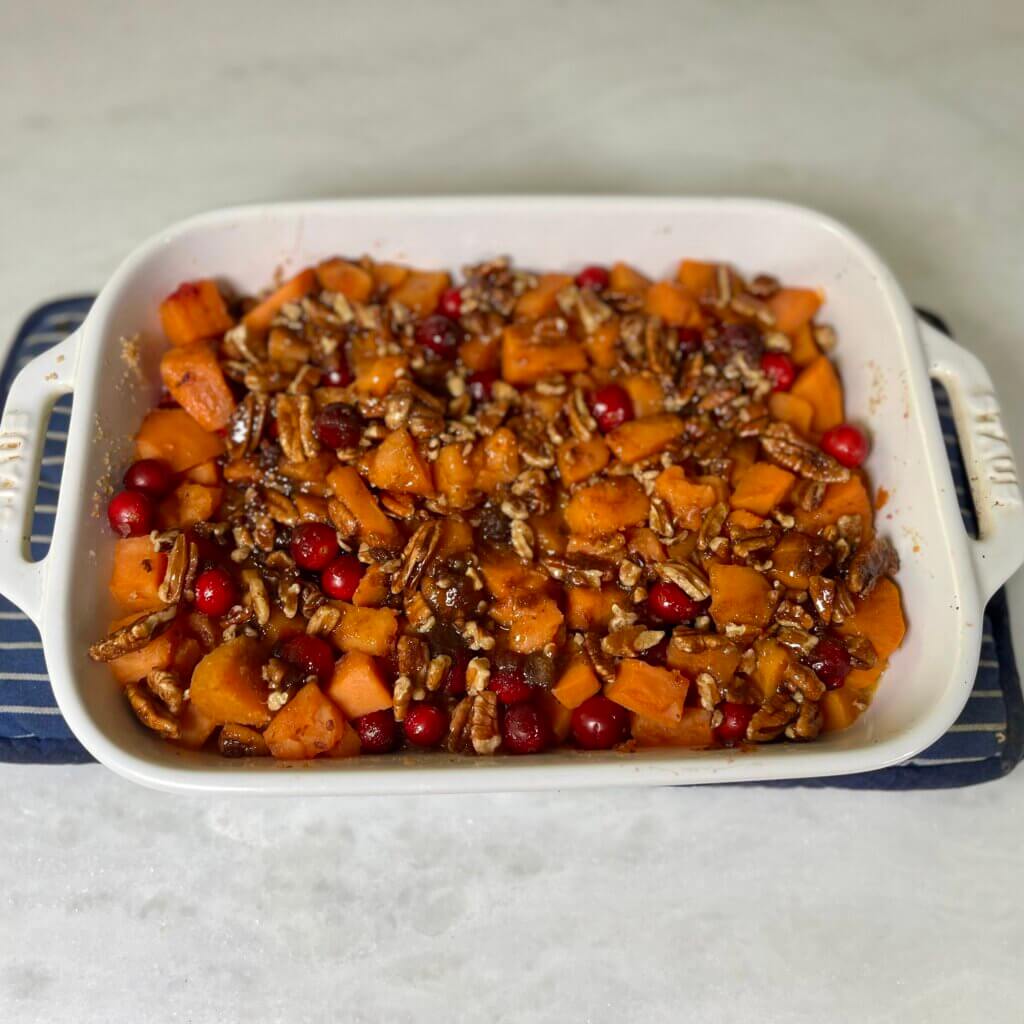 Cubed par-boiled sweet potatoes mixed with fresh cranberries, pecans and brown sugar in a white casserole dish