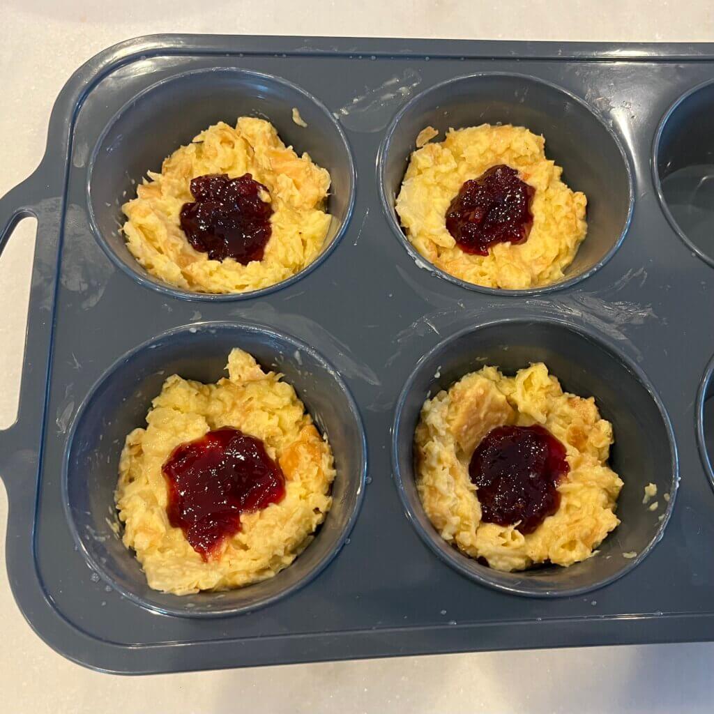 Croissant cupcake mixture in a cupcake pan with New Canaan Farms Cherry Preserves spooned in the canter of each